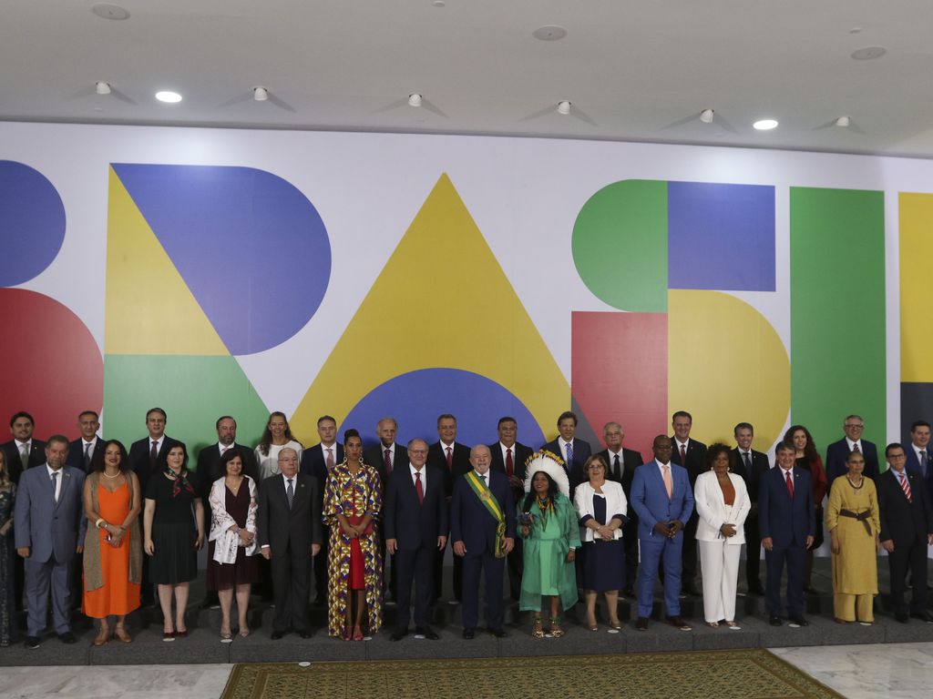 Foto oficial de Lula com os ministros no dia da posse. Eles estão à frente do logo do novo governo: a palavra Brasil, grafada com letras coloridas