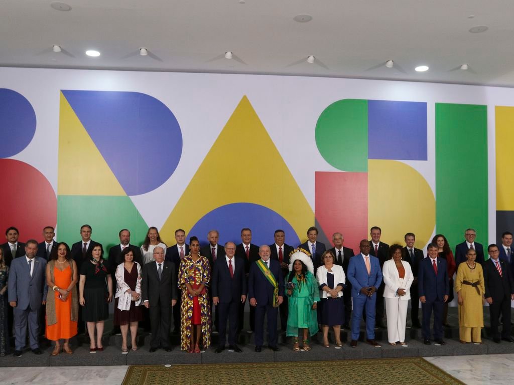 Foto oficial de Lula com os ministros no dia da posse. Eles estão à frente do logo do novo governo: a palavra Brasil, grafada com letras coloridas